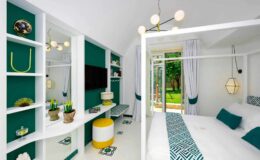 Modern bedroom interior featuring a four-poster bed, vibrant teal walls, stylish lighting fixtures, and a cozy seating area with garden views. Decor includes decorative plants and contemporary furniture, creating a chic and inviting atmosphere.