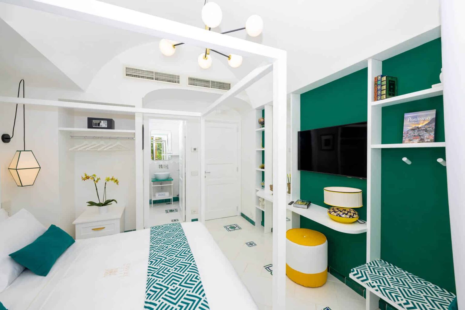 Modern hotel room featuring a bright, airy design with white walls, teal accents, and stylish decor. The room includes a comfortable bed, a flat-screen TV, and a cozy seating area, ideal for relaxation. | Only on SopranoVillas