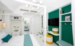 Modern hotel room featuring a bright, airy design with white walls, teal accents, and stylish decor. The room includes a comfortable bed, a flat-screen TV, and a cozy seating area, ideal for relaxation.
