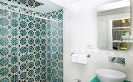 Modern bathroom with a stylish glass shower featuring turquoise patterned tiles, a sleek mirror above a contemporary sink, and white towels hanging on the wall.