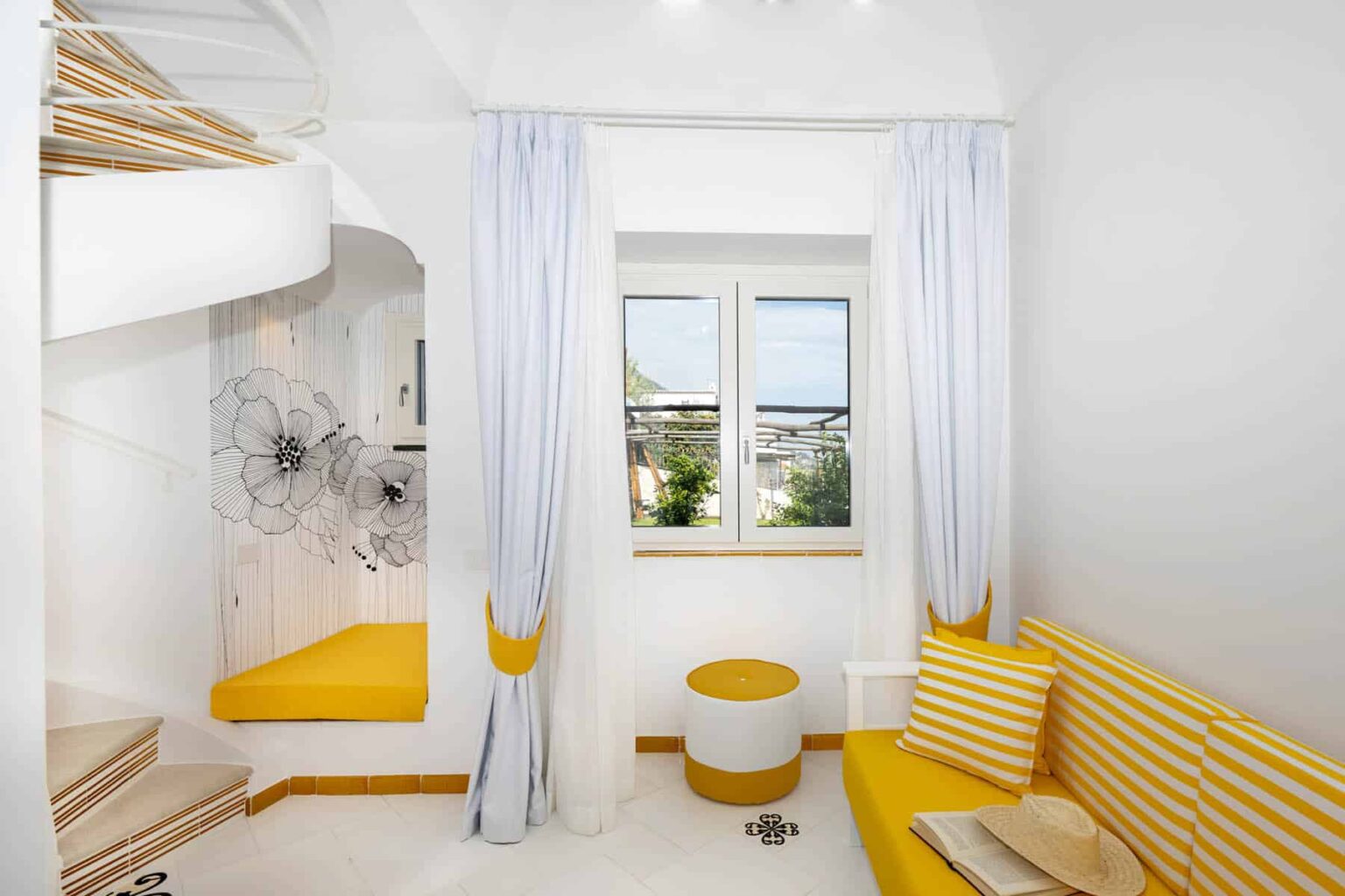 Bright and modern interior of a cozy room featuring white walls, yellow accents, a comfortable seating area with striped cushions, and a large window allowing natural light. The space includes a unique staircase and decorative elements, creating an inviting atmosphere. | Only on SopranoVillas