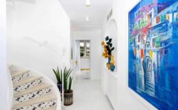 Bright and modern hallway featuring a spiral staircase, vibrant artwork on the wall, and decorative plants, creating an inviting atmosphere in a contemporary home.