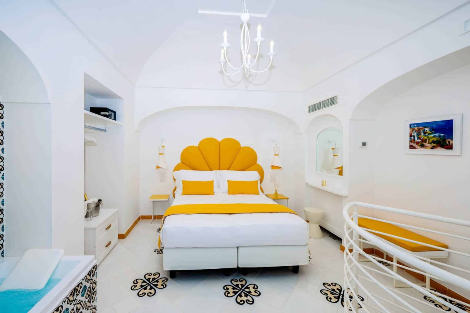 Bright and modern hotel bedroom featuring a white color scheme with yellow accents, a stylish shell-shaped headboard, elegant chandelier, and decorative black and white patterned flooring. Ideal for a luxurious stay. | Only on SopranoVillas