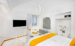 Bright and airy hotel room featuring white walls, a cozy bed with an orange accent, a flat-screen TV, and a window with scenic views. The room includes a stylish bathtub and modern decor, creating a relaxing atmosphere.