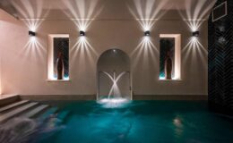 Indoor spa area featuring a tranquil pool with water features, illuminated by stylish wall sconces and ambient lighting, creating a serene atmosphere for relaxation and wellness.