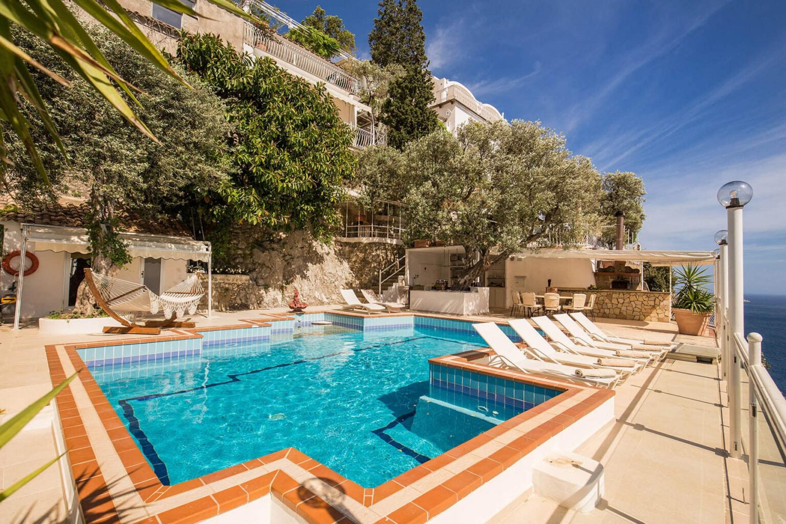 Luxurious outdoor pool area with sun loungers and lush greenery, overlooking a scenic view. Ideal for relaxation and leisure in a tranquil setting. | Only on SopranoVillas