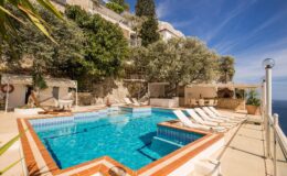 Luxurious outdoor pool area with sun loungers and lush greenery, overlooking a scenic view. Ideal for relaxation and leisure in a tranquil setting.