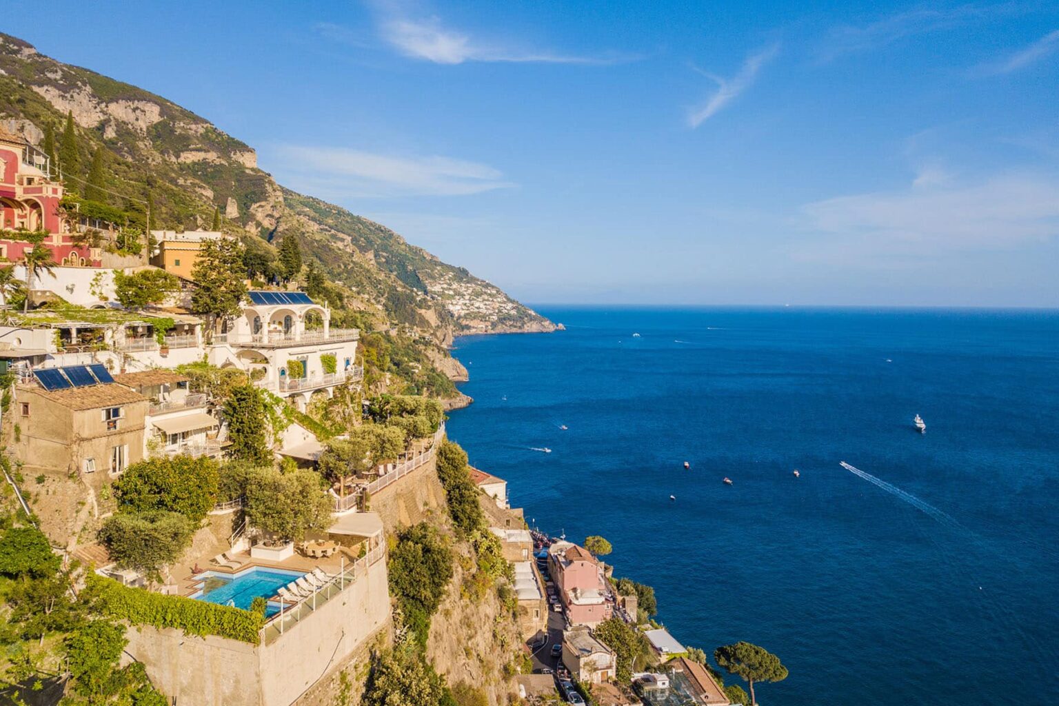 Scenic view of Positano, Italy, showcasing colorful cliffside villas overlooking the turquoise Mediterranean Sea with sailboats in the distance. | Only on SopranoVillas