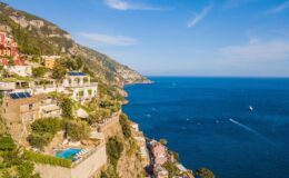 Scenic view of Positano, Italy, showcasing colorful cliffside villas overlooking the turquoise Mediterranean Sea with sailboats in the distance.