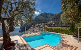 Luxurious outdoor pool with stunning mountain and sea views, surrounded by lush greenery and a sun terrace, ideal for relaxation and leisure in a coastal villa setting.