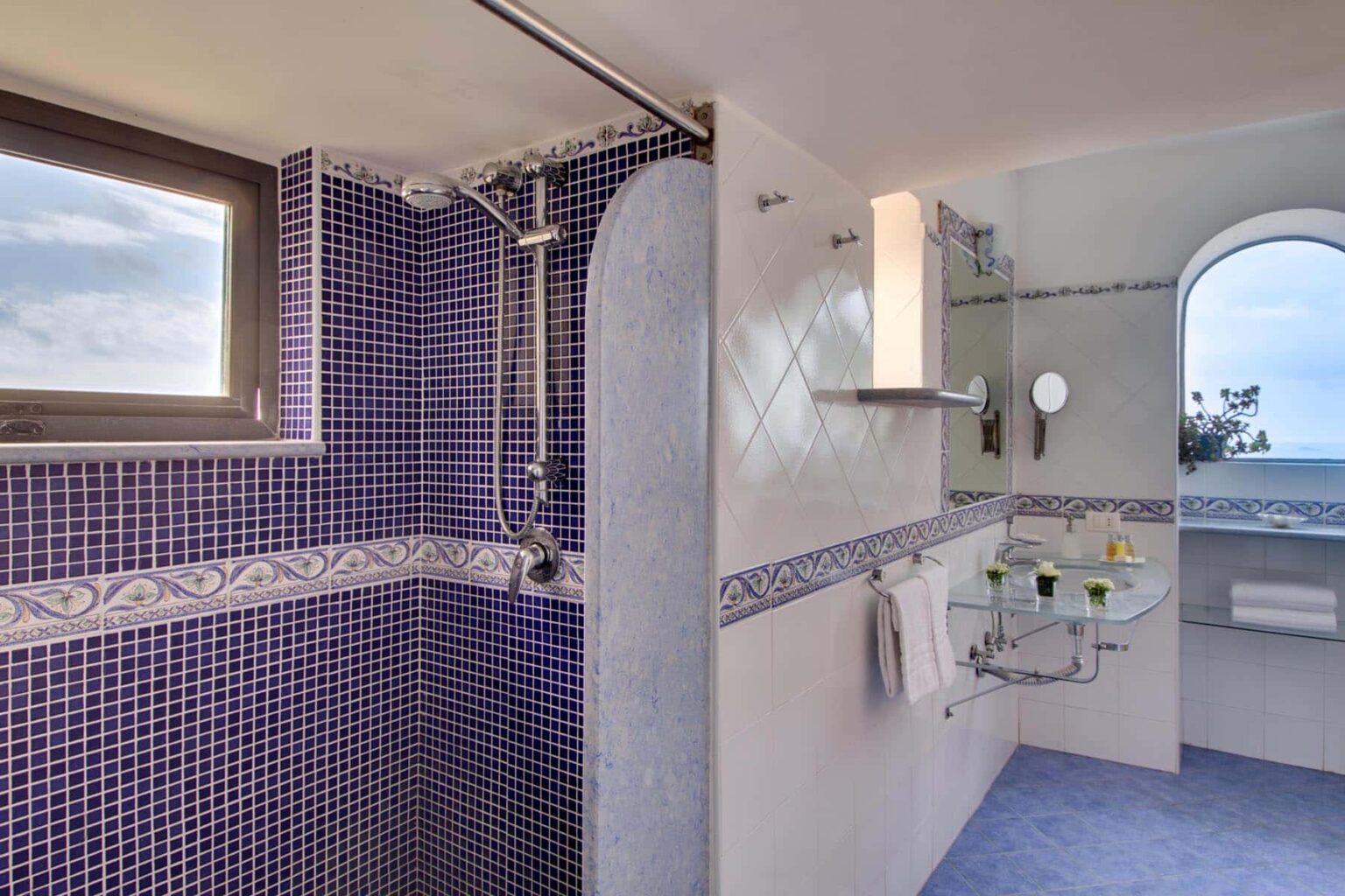 Modern bathroom with purple tile accents, featuring a spacious walk-in shower, large window for natural light, and elegant fixtures. The design emphasizes a clean aesthetic and ocean views. | Only on SopranoVillas