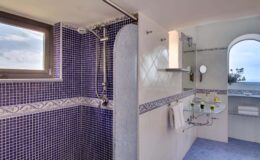 Modern bathroom with purple tile accents, featuring a spacious walk-in shower, large window for natural light, and elegant fixtures. The design emphasizes a clean aesthetic and ocean views.