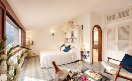 Bright and airy hotel room featuring a queen-sized bed, elegant decor, and large windows offering scenic views. The space includes a cozy seating area, stylish furnishings, and natural light enhancing the tranquil atmosphere. Ideal for relaxation and comfort during a getaway.
