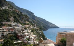 Panoramic view of Positano, Italy, showcasing colorful cliffside houses against a backdrop of mountains and the Mediterranean Sea under a clear blue sky. Ideal for travel and tourism content.