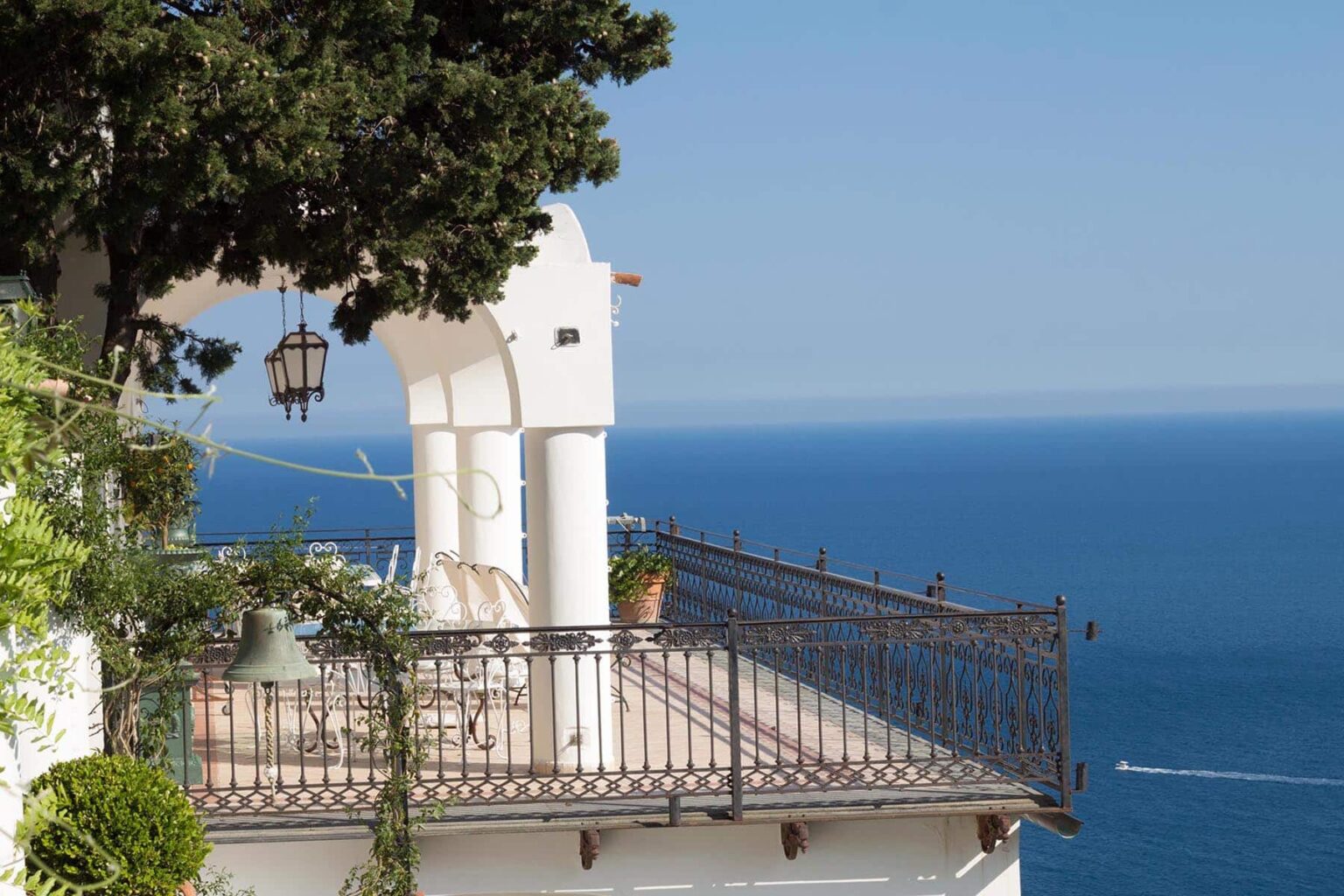 Scenic ocean view from a balcony with white architecture and lush greenery, overlooking a calm blue sea. | Only on SopranoVillas