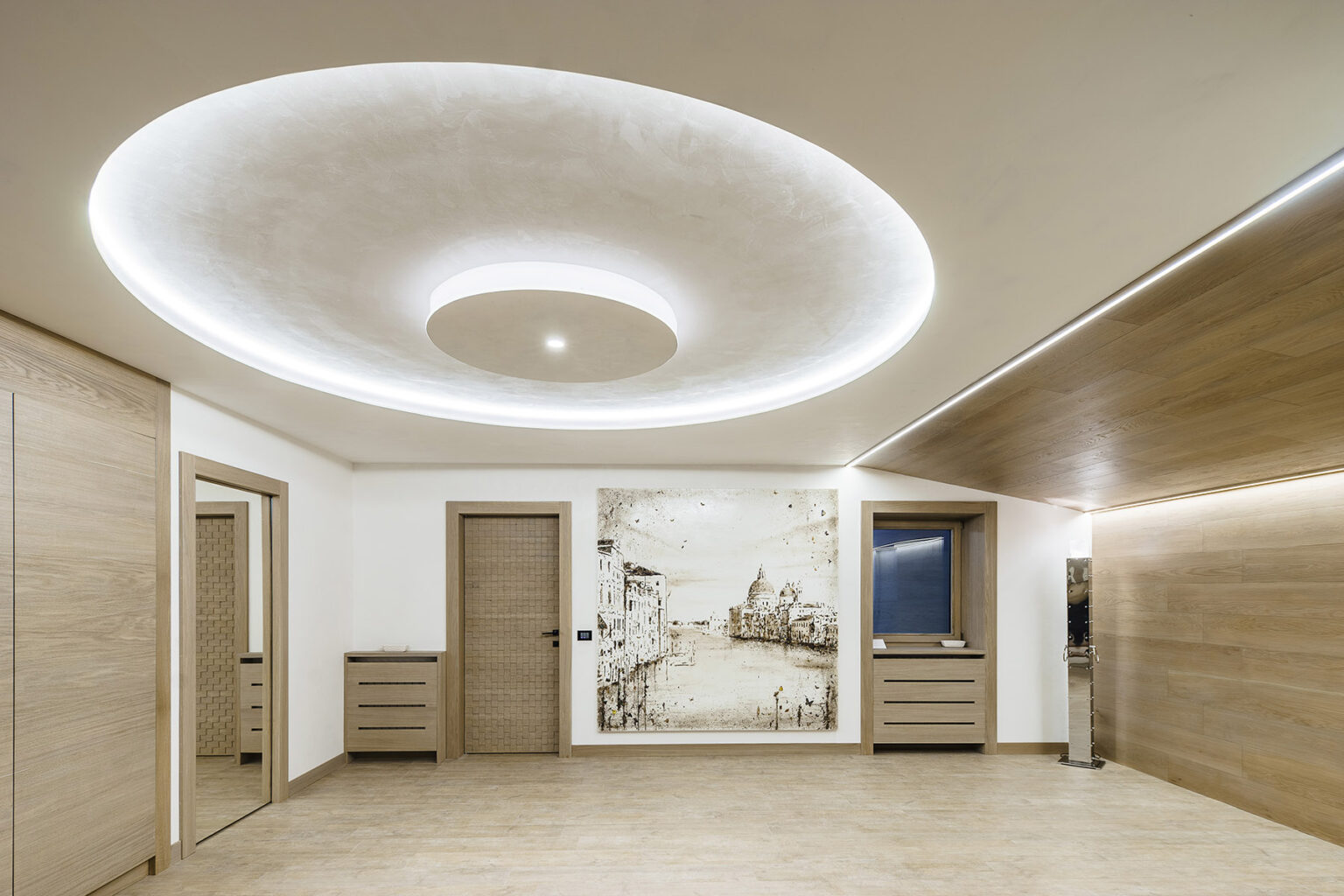 Modern interior design featuring a spacious room with wooden accents, a circular ceiling light, and a decorative wall art piece. The room includes light-colored walls and a minimalist aesthetic, showcasing sleek furniture and a contemporary style. | Only on SopranoVillas