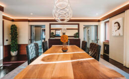 Modern dining room featuring a large wooden table, elegant leather chairs, and contemporary lighting fixtures. The room is accentuated with decorative plants and artwork, creating a stylish and inviting atmosphere.