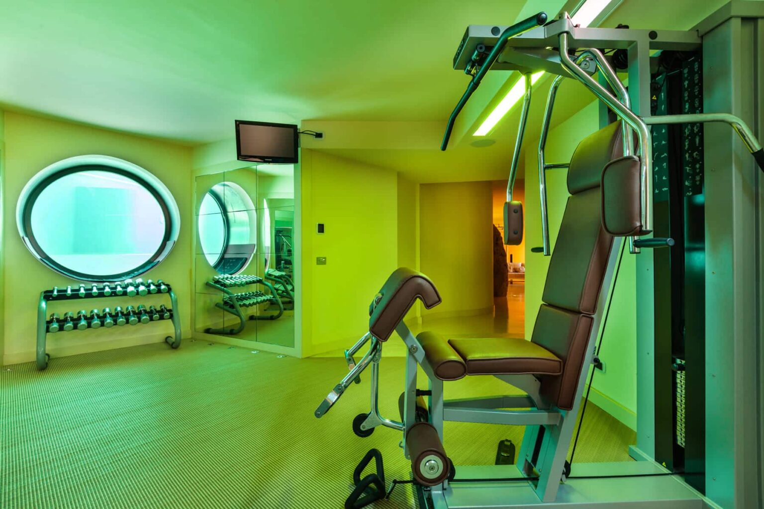 Modern gym interior featuring a multi-station weight machine, free weights, and vibrant green lighting. | Only on SopranoVillas