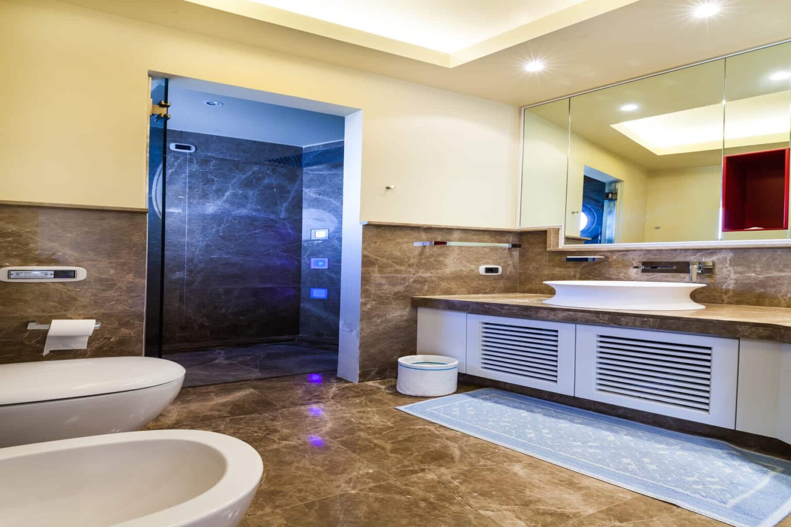 Modern bathroom interior featuring a spacious layout, stylish fixtures, a walk-in shower with ambient lighting, a sleek vanity with a large mirror, and elegant stone flooring. | Only on SopranoVillas