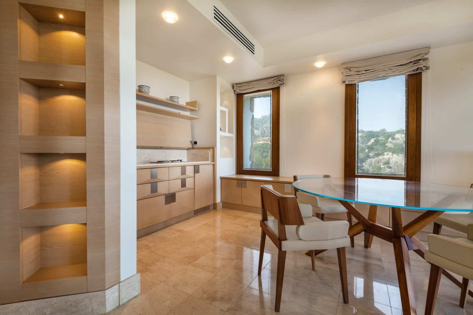 Modern kitchen and dining area featuring sleek cabinetry, a glass dining table, and large windows providing natural light. The space showcases a minimalist design with warm tones and elegant furnishings. | Only on SopranoVillas