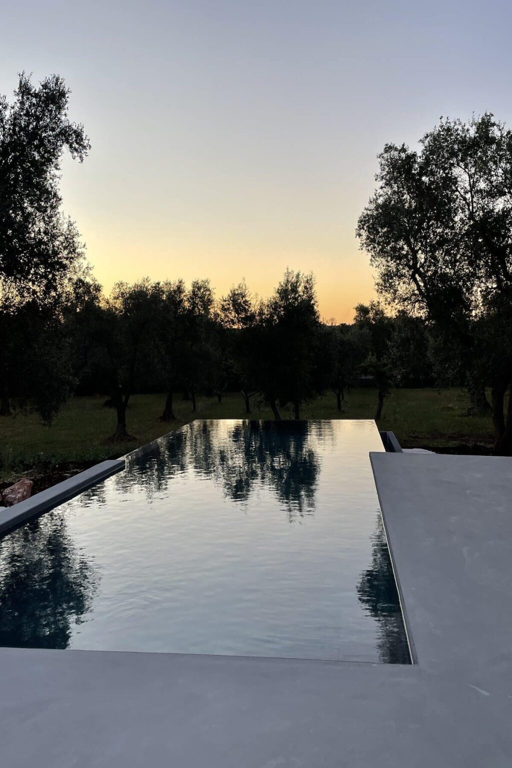 Serene infinity pool reflecting the sunset, surrounded by olive trees in a tranquil outdoor setting. | Only on SopranoVillas