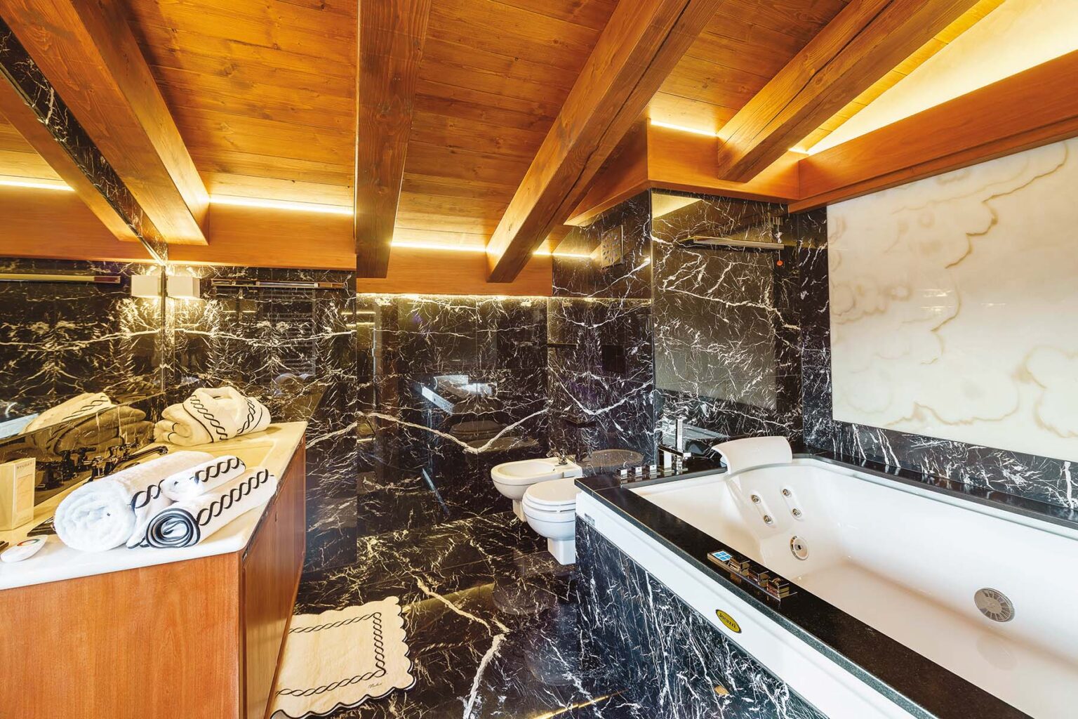 Luxurious modern bathroom featuring dark marble walls, wooden ceiling beams, a freestanding bathtub, and elegant fixtures, perfect for a spa-like experience. | Only on SopranoVillas