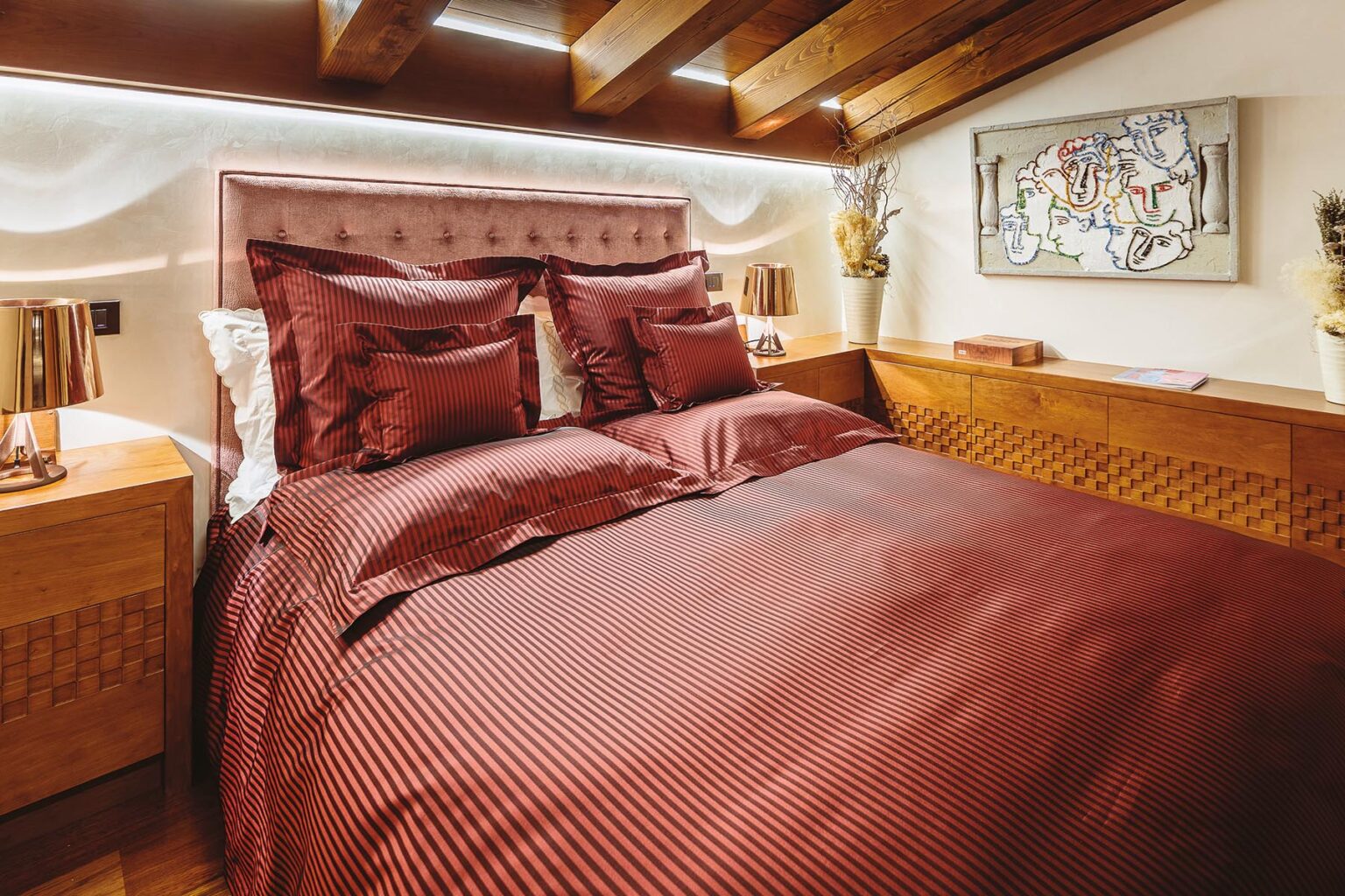 Luxurious bedroom featuring a king-size bed with rich burgundy bedding and decorative pillows, complemented by wooden furniture and warm lighting. | Only on SopranoVillas