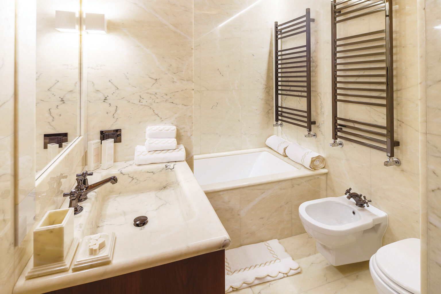Modern bathroom interior featuring a marble countertop, a bathtub, a bidet, and a towel rack. The space is well-lit and elegantly designed, with neatly arranged towels and a clean aesthetic. Ideal for showcasing luxury bathroom design. | Only on SopranoVillas