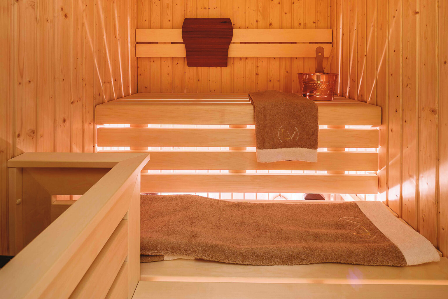 Interior view of a wooden sauna featuring warm lighting, a wooden bench, and towels, creating a relaxing atmosphere for wellness and relaxation. | Only on SopranoVillas