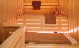 Interior view of a wooden sauna featuring warm lighting, a wooden bench, and towels, creating a relaxing atmosphere for wellness and relaxation.
