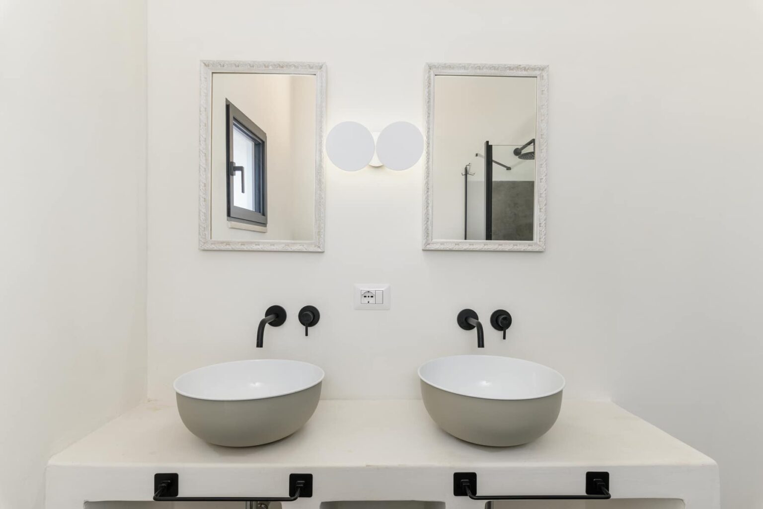 Modern bathroom design featuring a double vanity with two round, gray basins, framed mirrors above, and stylish wall-mounted faucets. The minimalist decor is complemented by a neutral color palette and natural light. | Only on SopranoVillas