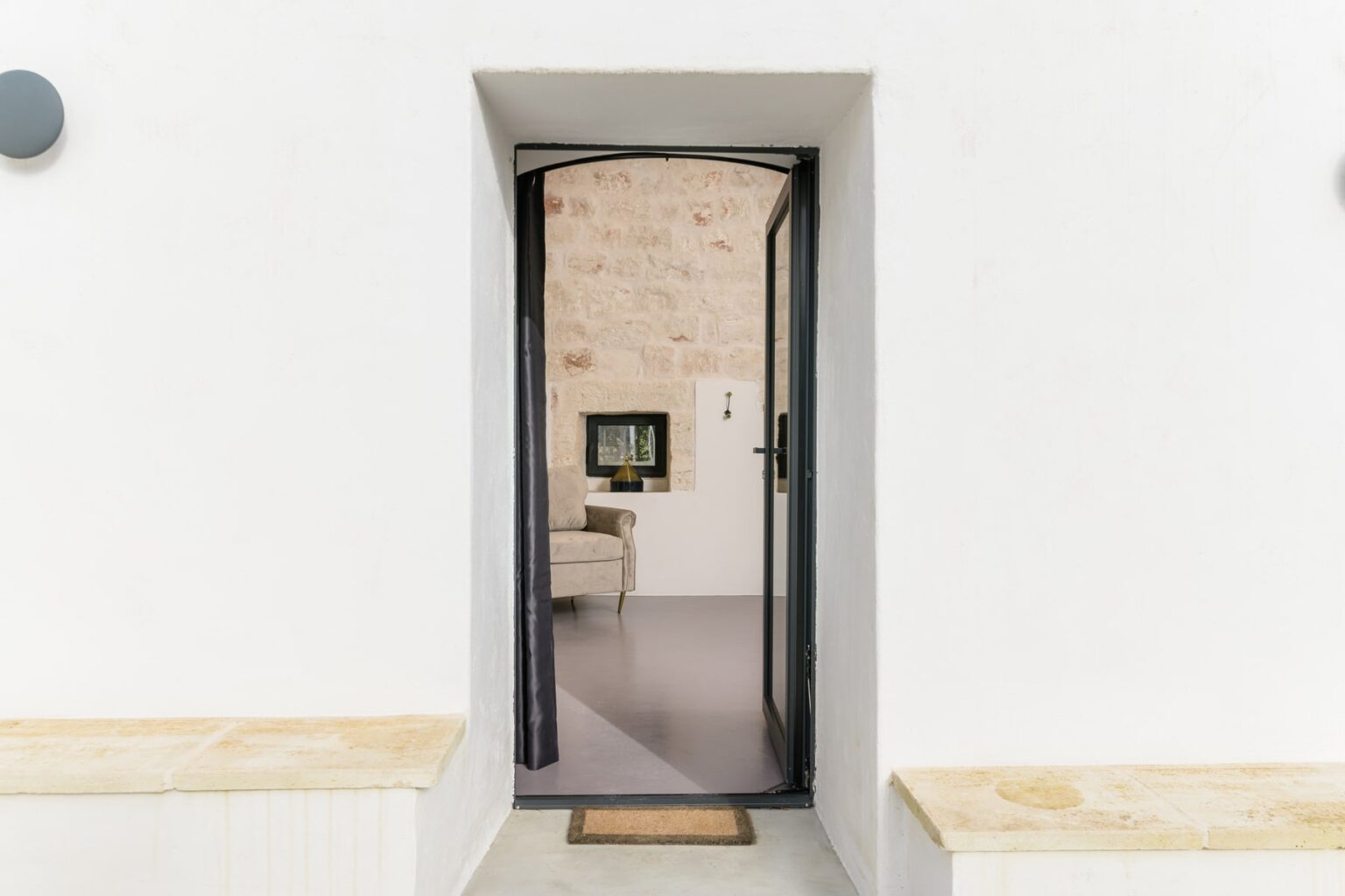 Modern entrance door with a sleek black frame, leading into a stylish interior featuring a stone wall and contemporary furniture, ideal for home design inspiration. | Only on SopranoVillas