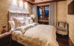 Cozy and elegant bedroom featuring a plush bed with soft bedding, stylish headboard, and ambient lighting. The room includes large windows with scenic views, tasteful curtains, and a comfortable armchair, creating a welcoming atmosphere for relaxation.