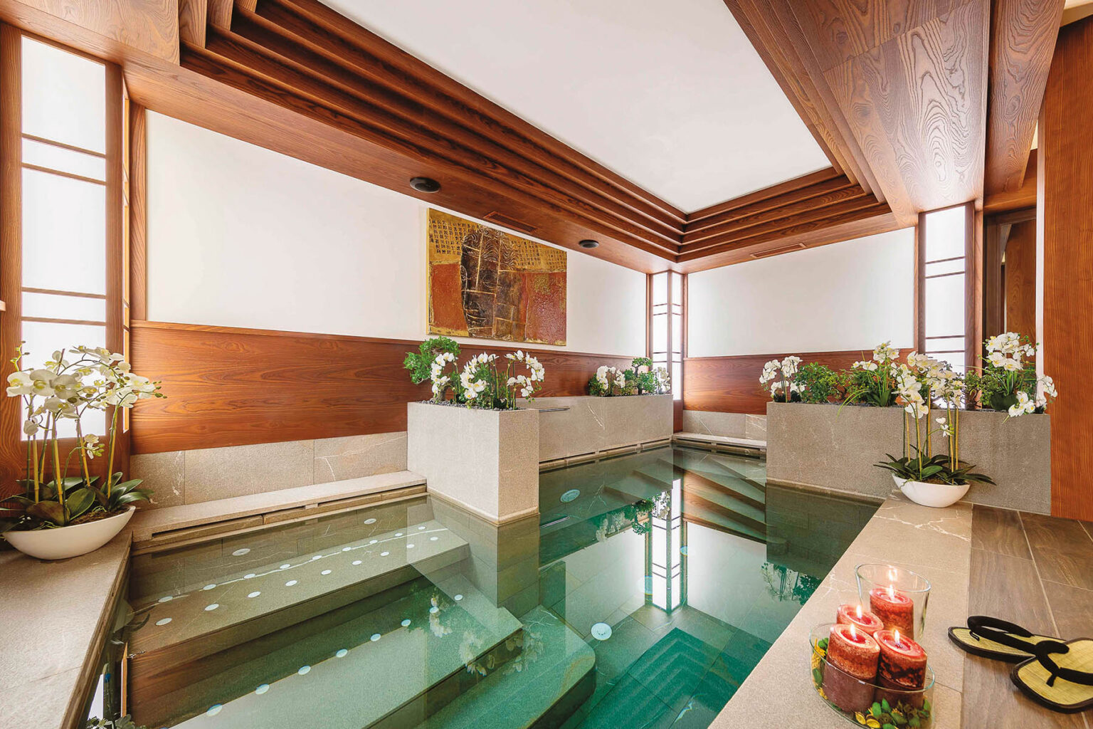 Luxurious indoor spa featuring a tranquil pool, elegant wooden accents, and lush greenery. The space is adorned with candles and stylish footwear, creating a serene atmosphere for relaxation and rejuvenation. | Only on SopranoVillas
