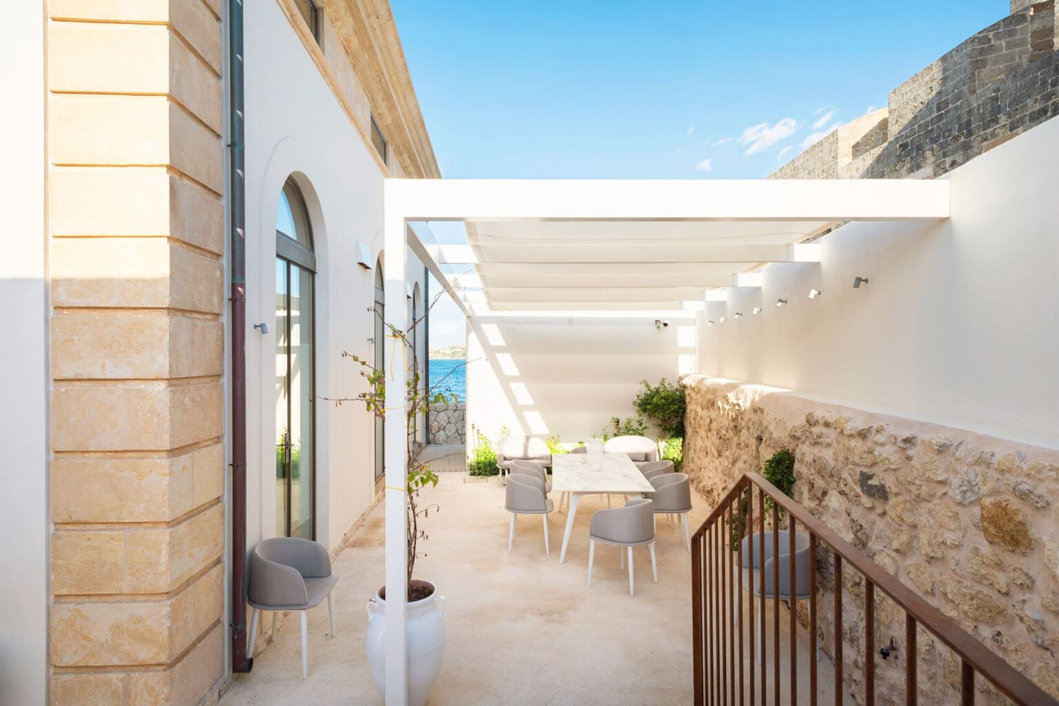Modern outdoor dining area with a pergola, featuring a light color palette, contemporary furniture, and views of the sea. Ideal for alfresco meals and relaxation in a coastal setting. | Only on SopranoVillas