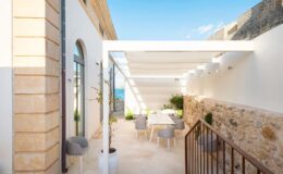 Modern outdoor dining area with a pergola, featuring a light color palette, contemporary furniture, and views of the sea. Ideal for alfresco meals and relaxation in a coastal setting.