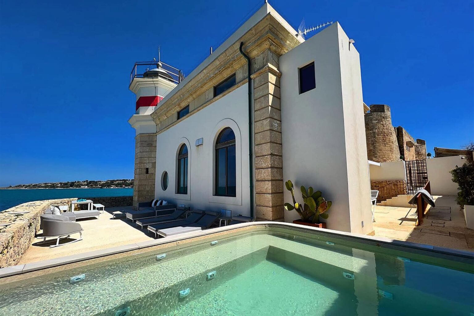 Lighthouse villa by the sea with a swimming pool, featuring modern outdoor seating and clear blue skies. | Only on SopranoVillas