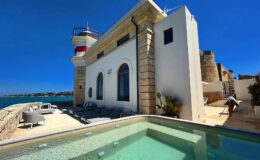 Lighthouse villa by the sea with a swimming pool, featuring modern outdoor seating and clear blue skies.