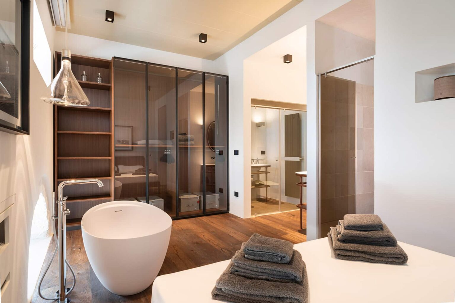 Modern bathroom interior featuring a freestanding bathtub, elegant shelving, and stylish towels neatly arranged on a countertop, with glass partitions and contemporary lighting. | Only on SopranoVillas