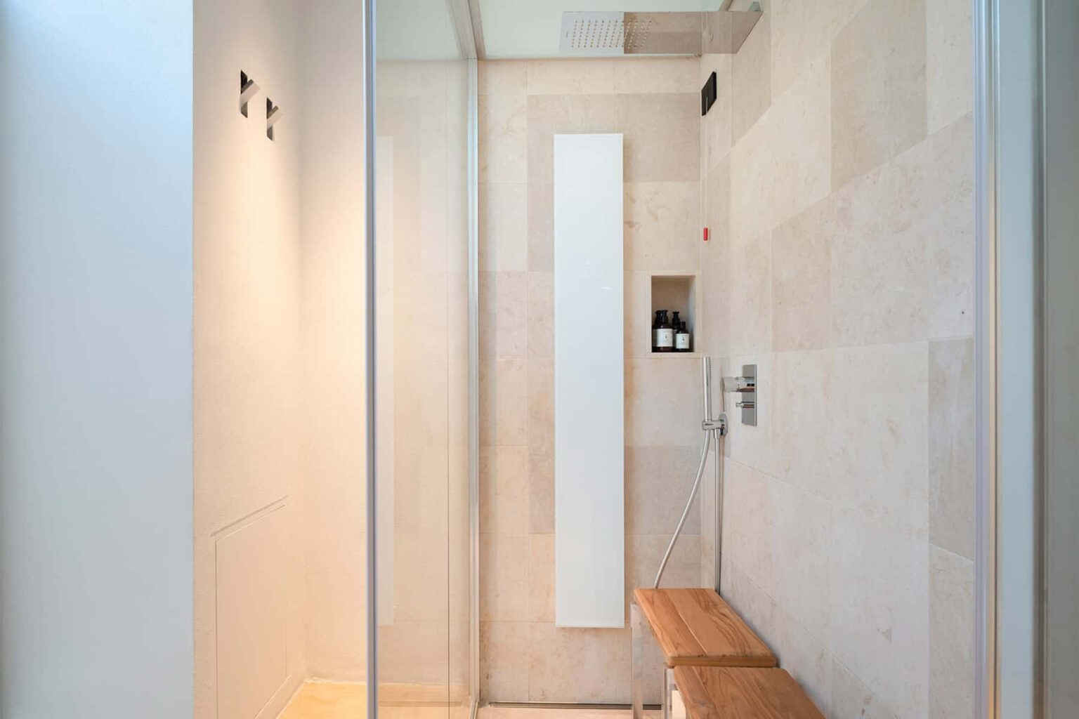 Modern shower interior featuring glass walls, natural stone tiles, a wooden bench, and minimalist design elements. Ideal for showcasing contemporary bathroom aesthetics. | Only on SopranoVillas