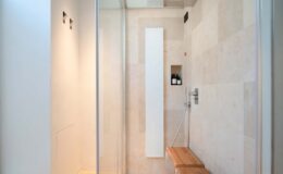 Modern shower interior featuring glass walls, natural stone tiles, a wooden bench, and minimalist design elements. Ideal for showcasing contemporary bathroom aesthetics.