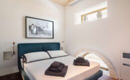 Modern bedroom featuring a comfortable bed with neatly arranged towels, minimalist decor, and a large artwork on the wall, illuminated by natural light from a window.