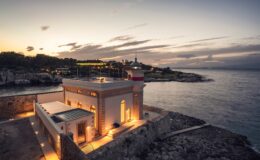 Scenic view of a historic lighthouse at sunset, illuminated against the backdrop of the ocean and rocky coastline, highlighting its architectural features and tranquil surroundings.