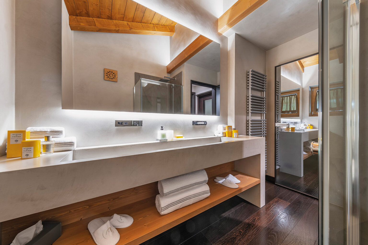 Modern bathroom interior featuring a sleek vanity with a large mirror, ambient lighting, and neatly arranged towels. The space showcases wooden accents, a glass shower, and contemporary decor, creating a stylish and inviting atmosphere. | Only on SopranoVillas