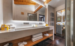 Modern bathroom interior featuring a sleek vanity with a large mirror, ambient lighting, and neatly arranged towels. The space showcases wooden accents, a glass shower, and contemporary decor, creating a stylish and inviting atmosphere.