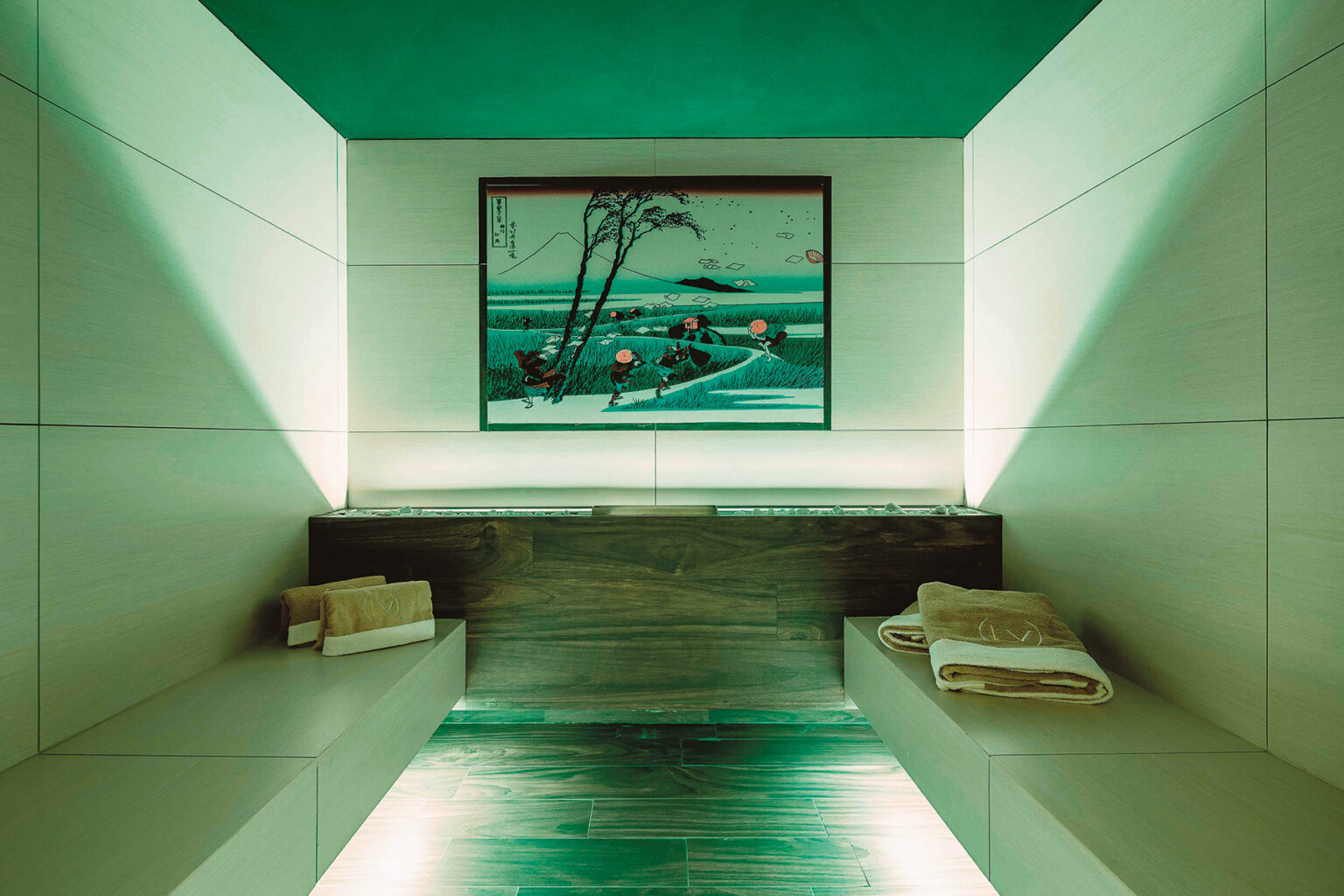 Modern spa interior featuring minimalist design, calming green lighting, and a serene landscape painting on the wall, with two neatly arranged towels on wooden benches. | Only on SopranoVillas