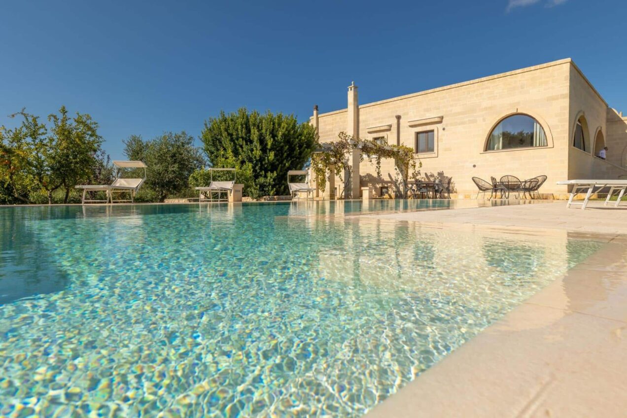 Luxurious outdoor pool with crystal-clear water, surrounded by lush greenery and a modern villa under a clear blue sky. Ideal for relaxation and leisure. | Only on SopranoVillas