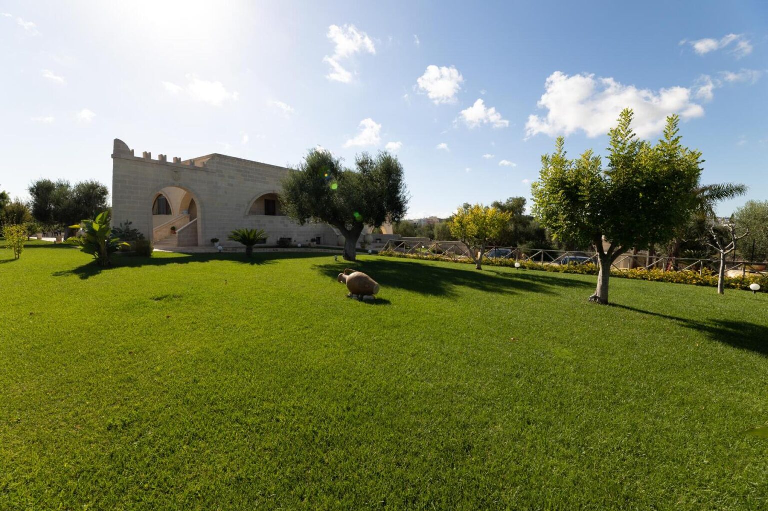 Scenic view of a well-maintained green lawn with trees and a historic building under a clear blue sky, highlighting the beauty of outdoor landscapes. | Only on SopranoVillas