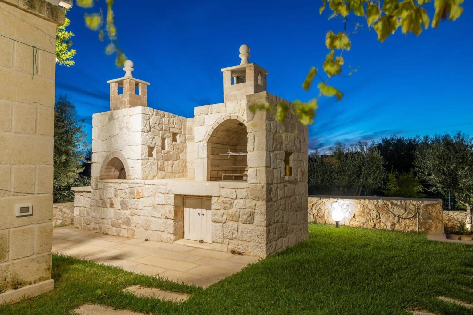 Stone building with arched windows and two towers, surrounded by green grass and illuminated by evening light, set against a clear blue sky. | Only on SopranoVillas