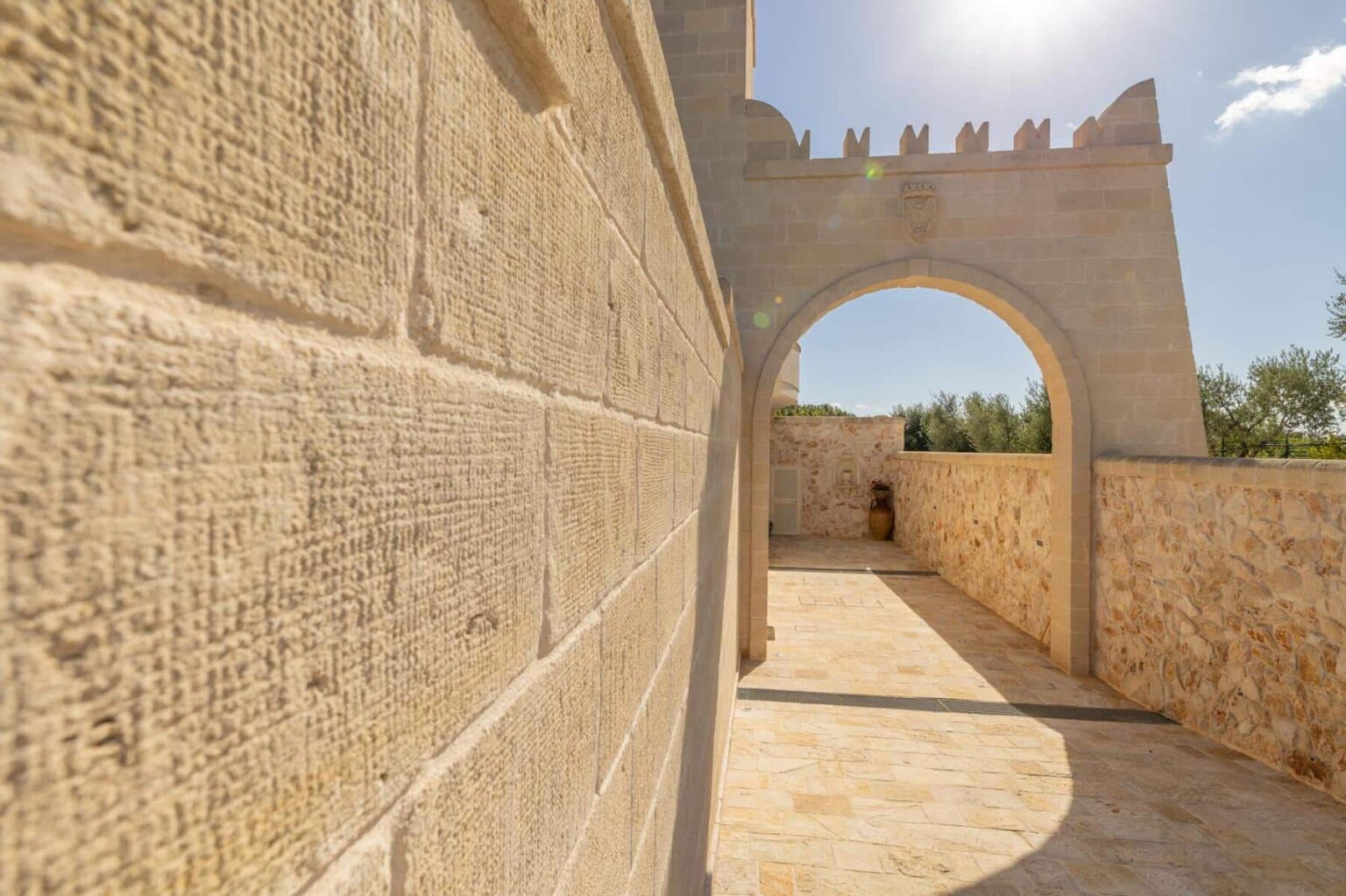 Stone wall and archway of an ancient structure, showcasing textured masonry and a sunny blue sky in the background. The image captures a corridor leading to an open space, highlighting historical architecture and natural light. | Only on SopranoVillas